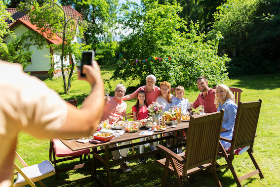 Leisure holidays people concept happy family having festive dinner summer garden party photographing by smartphone